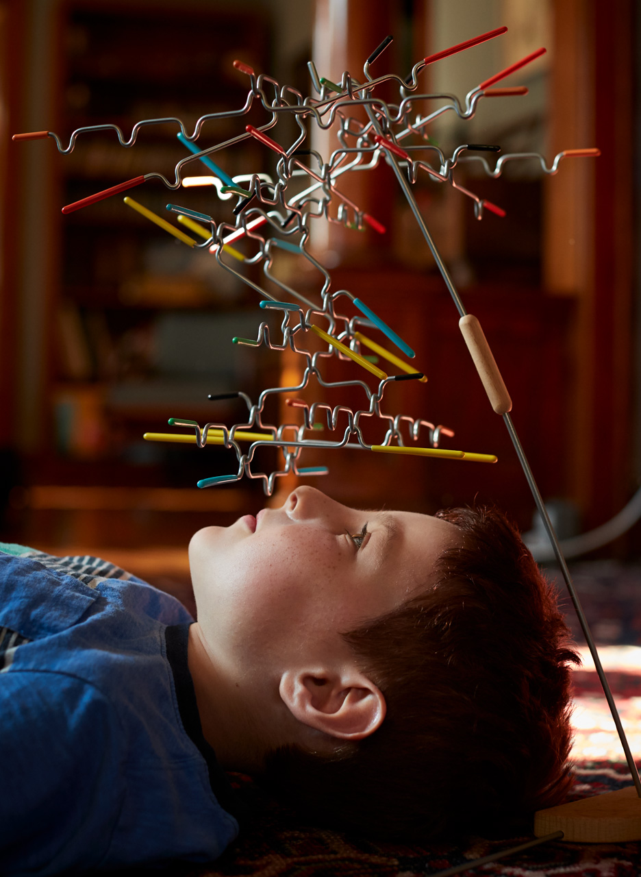 Boy laying beneith a balance stick puzzle | Childrens photography by Saverio Truglia