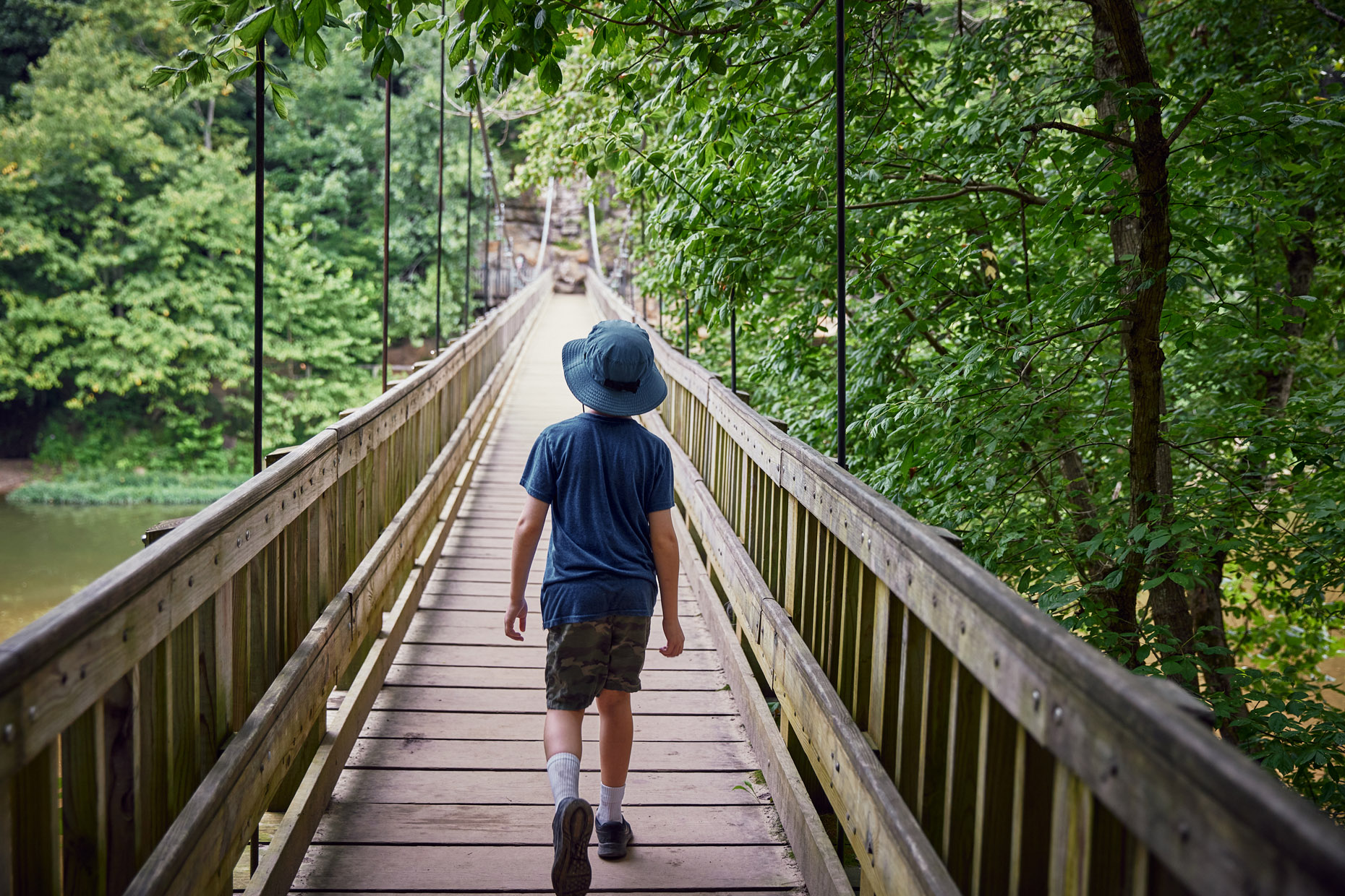 Boy walking across suspension bridge in the forest | Childrens photography by Saverio Truglia