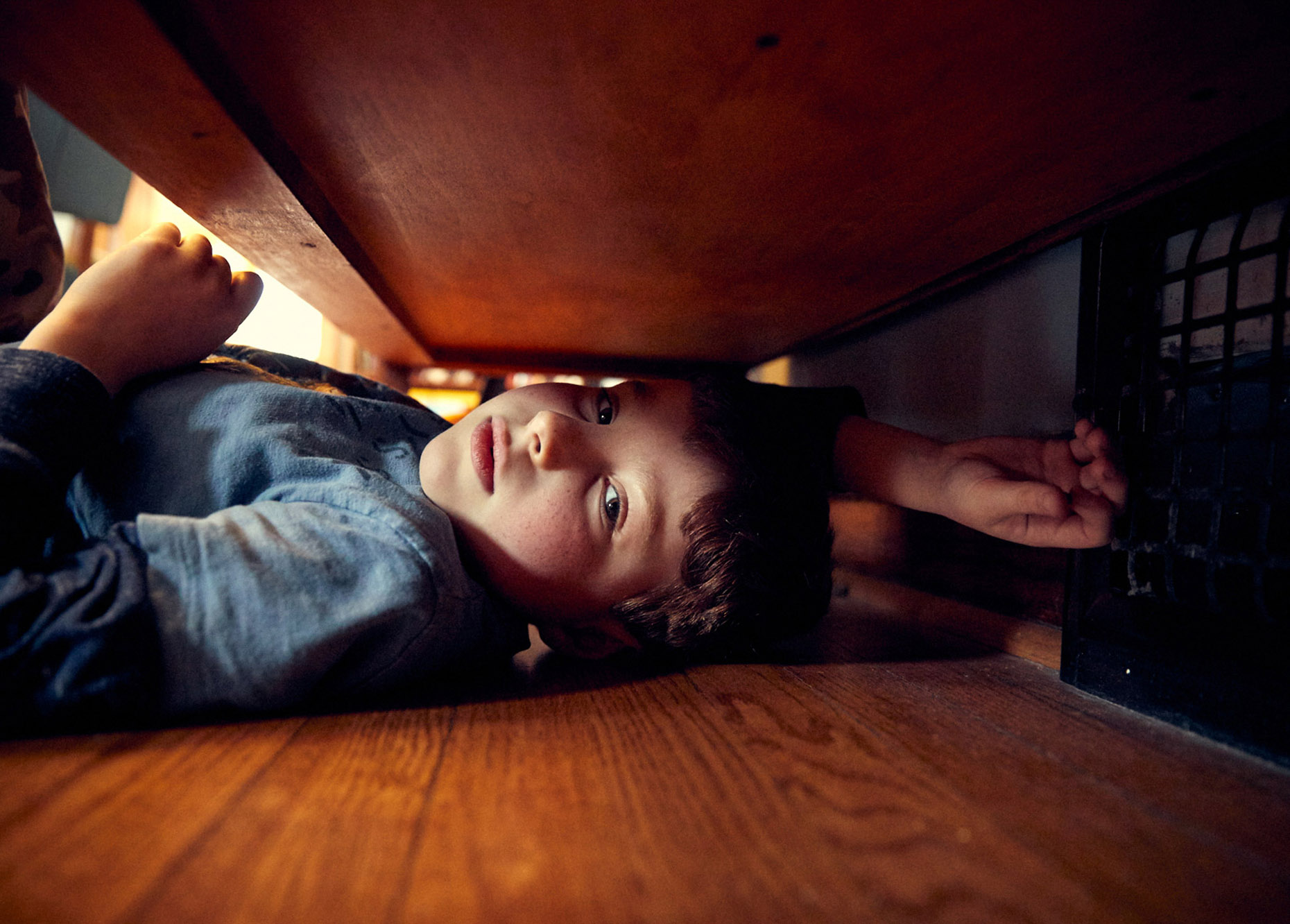 Young boy hiding under furniture | lifestyle photography by Saverio Truglia